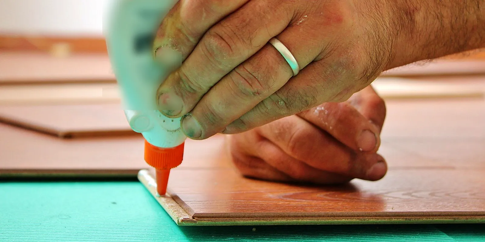 Mano aplicando adhesivo para madera sobre el canto de una tabla de piso laminado