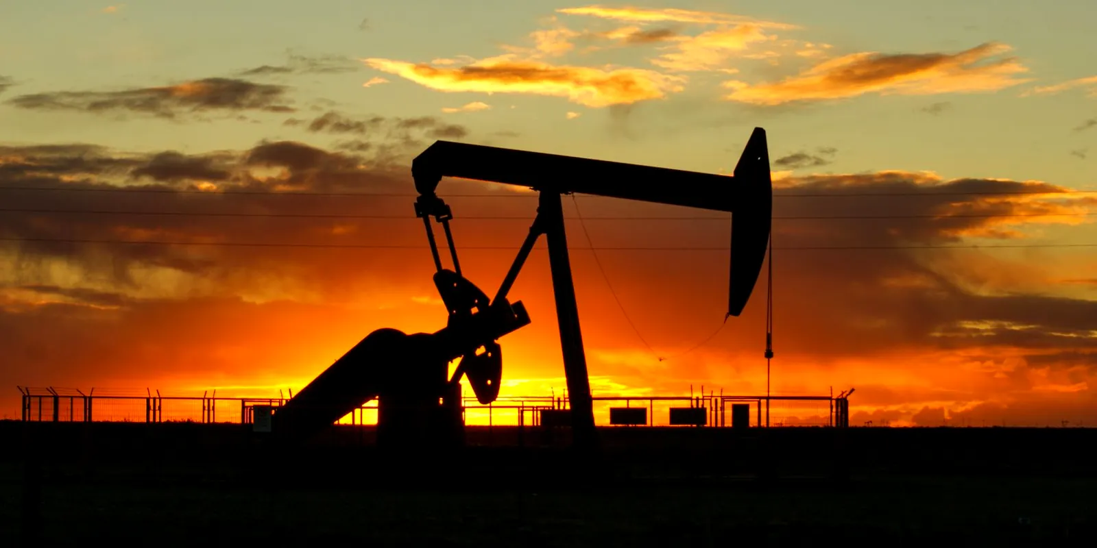 Bomba de extracción de petróleo (cigüeña) recortada contra el atardecer